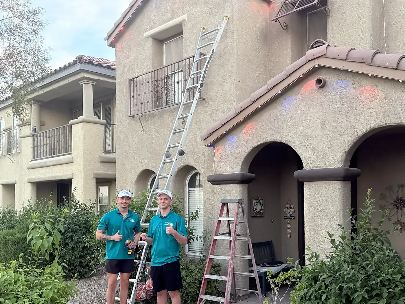 Two Magic Season Lighting installers giving a thumbs up beside their ladders