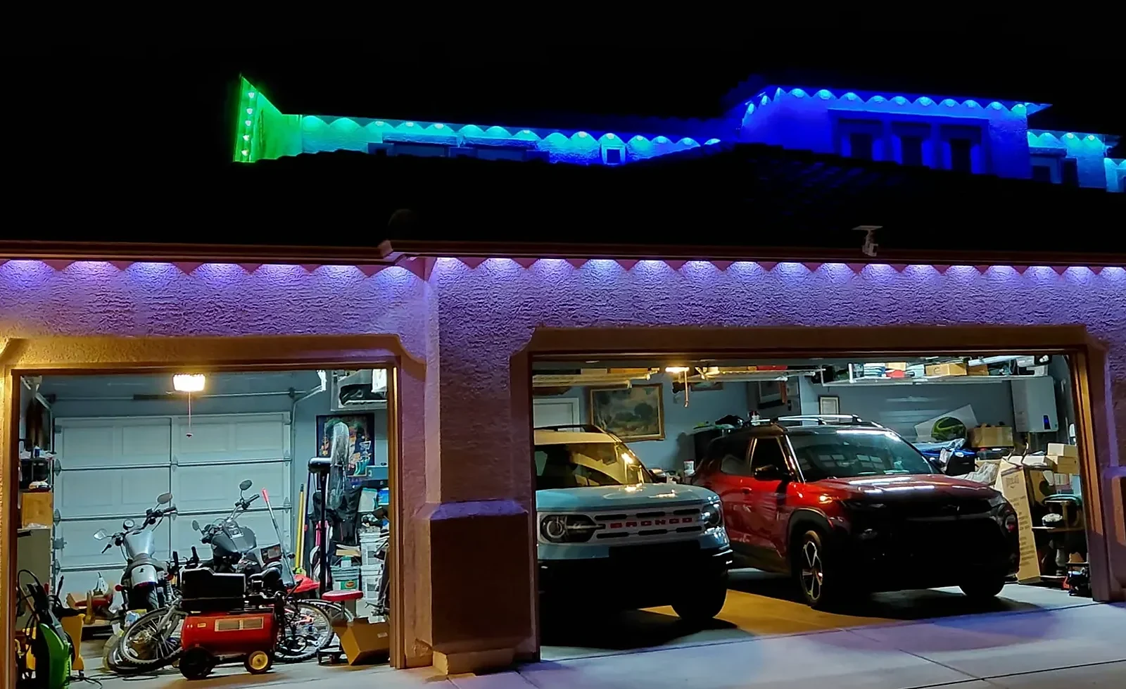 Home with blue and teal lights on the upper rooflines and purple scallops above three garage doors