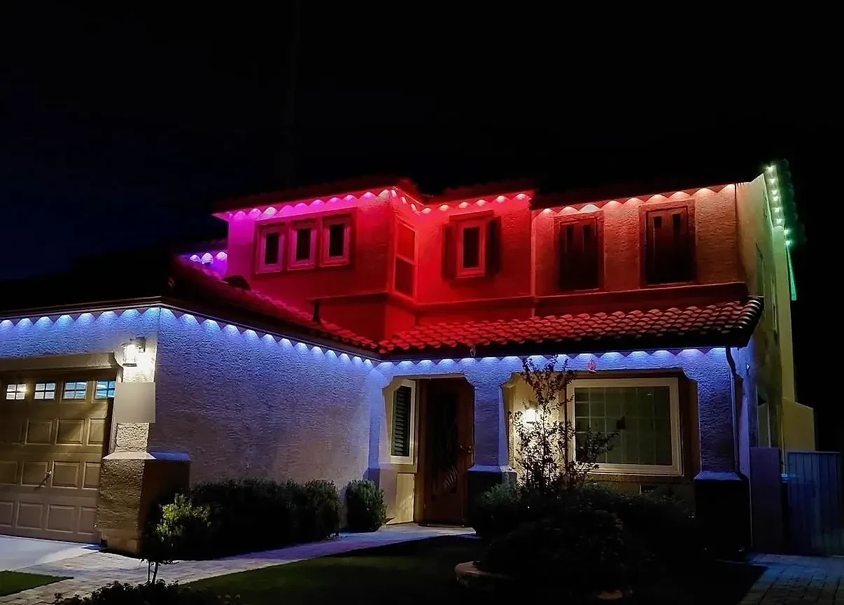 Two-story stucco home lit pink and red on the upper floor and blue along the lower roofline