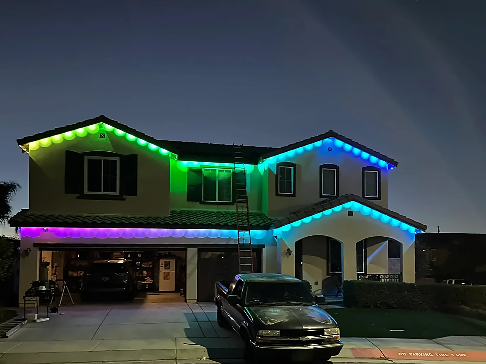 Two-story home with scalloped permanent lights fading from green to teal to purple